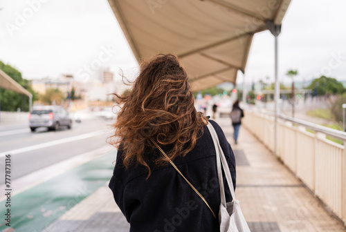 Back view of a young woman with long curly hair walking in the city photo