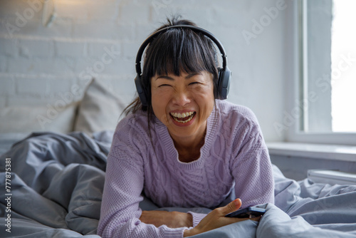Asian woman enjoying music in bed photo