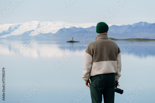 man with camera at glacier lake shoreline. Water reflection photo