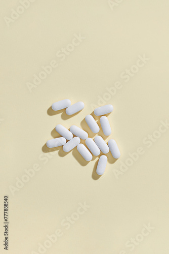 Many white pills on light yellow background, flat lay
