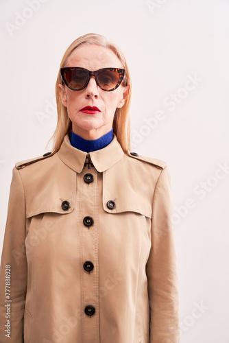 Stylish senior model wearing beige trench coat and vintage glasses 