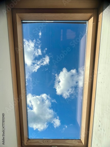 Window with blue sky and white clouds in the attic of the house