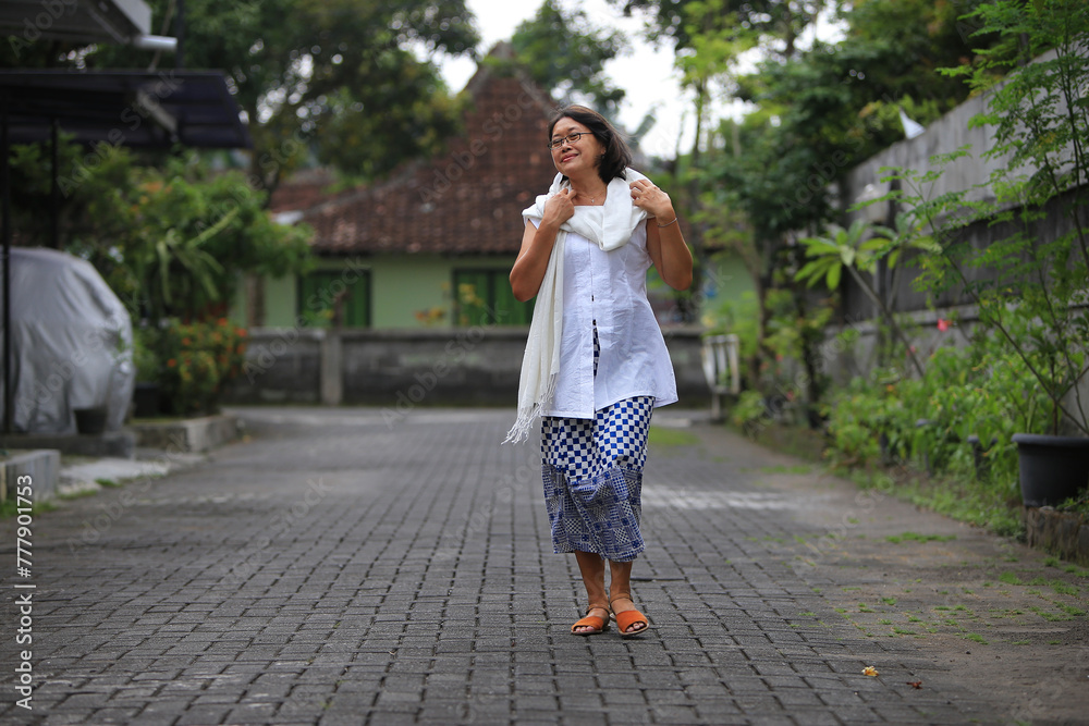 Adult woman wearing Batik casual attire walking along village alley