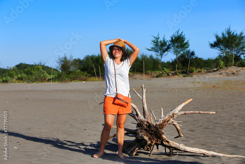 Asian female tourist stopping near washed tree on the beach photo