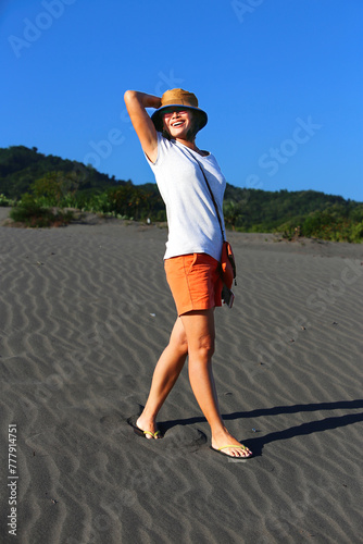 Woman enjoying the sunshine, walking along hot sandy beach photo