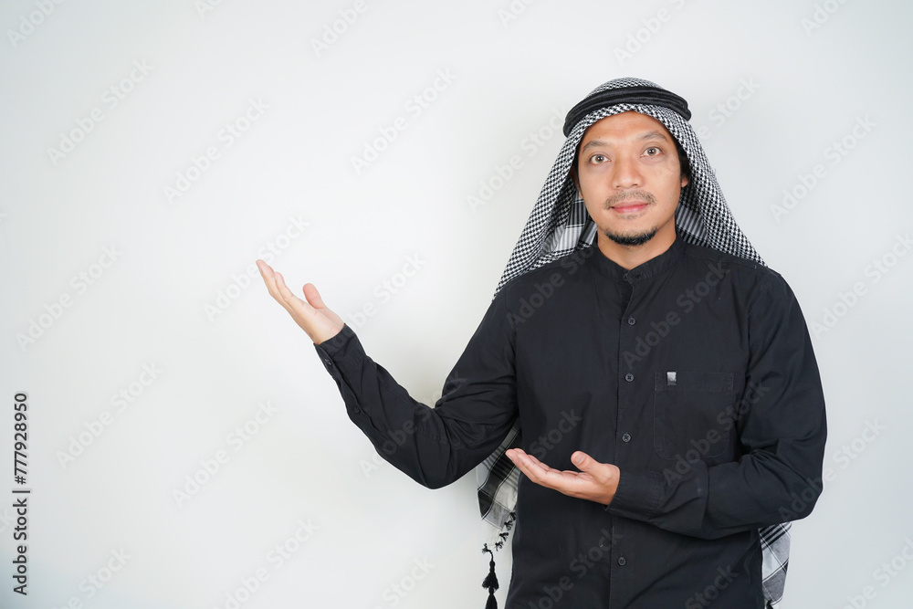 Cheerful Asian Muslim man wearing Arab turban sorban pointing hand finger at empty space on isolated Cheerful Asian Muslim man wearing Arab turban sorban pointing hand finger at empty space on isolated
