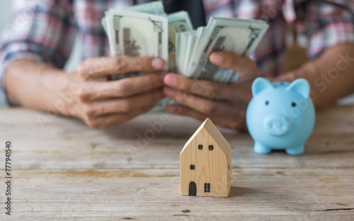 Hand's man holding money behind small house,saving concept,soft focus.