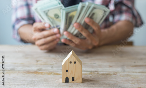 Hand's man holding money behind small house,saving concept,soft focus.