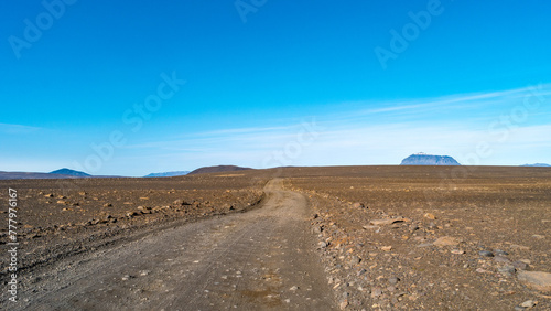 Dirt road near Herdubreid volcano in the lifeless volcanic desert in Highlands, with stones and rocks thrown by volcanic eruptions, Iceland, summer, blue sky.