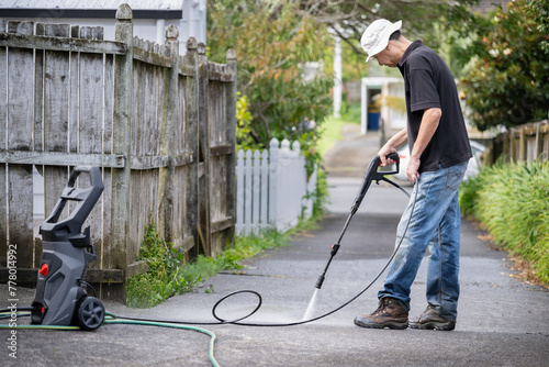 Man cleaning driveway using an electric water blaster.