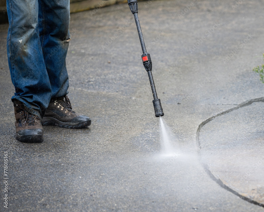 Worker cleaning pavement using an electric water blaster.