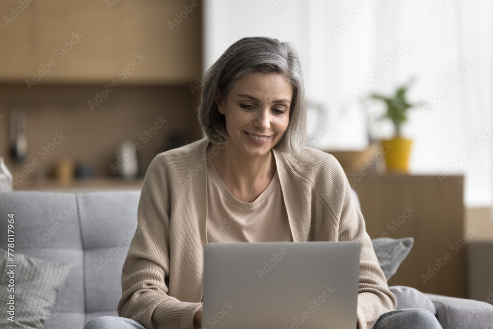Carefree pretty middle-aged woman relax at home, spend weekend time at home alone with laptop, looking at screen, chat, enjoy online communication, browse internet, use modern application, shopping Carefree pretty middle-aged woman relax at home, spend weekend time at home alone with laptop, looking at screen, chat, enjoy online communication, browse internet, use modern application, shopping