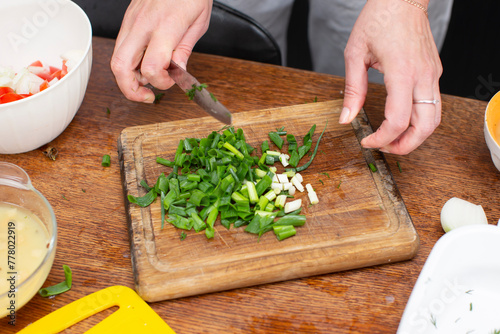 Hands chop green onions on a cutting board. Prepare vegetable salad.