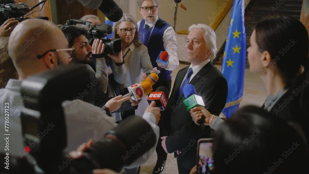 EU representative answers press questions and gives interview for TV breaking news. Senior consul surrounded by crowd of journalists. Political speech during press conference. State of the nation.