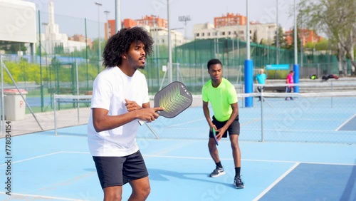 African young friends playing pickleball in an outdoor court in a sunny day