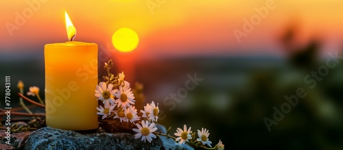 burning candle on the rock with daisies i sumer evening at sunset.  photo