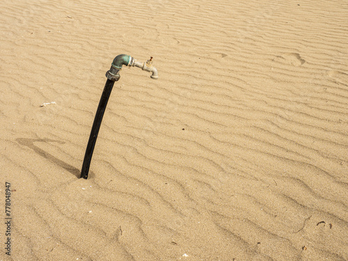 Tubo dell'acqua sulla sabbia. Rubinetto abbandonato: simbolo della crisi idrica e del degrado ambientale photo