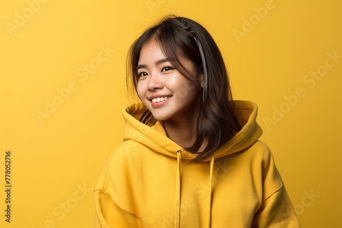 A woman in a yellow hoodie is smiling and looking at the camera