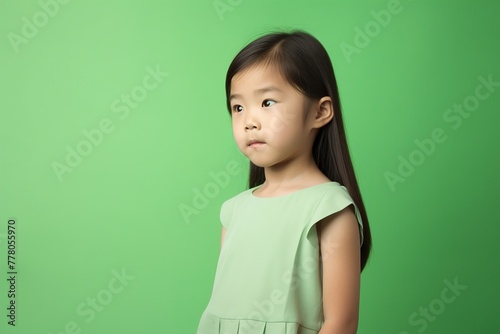 A young girl in a green dress is standing in front of a green wall