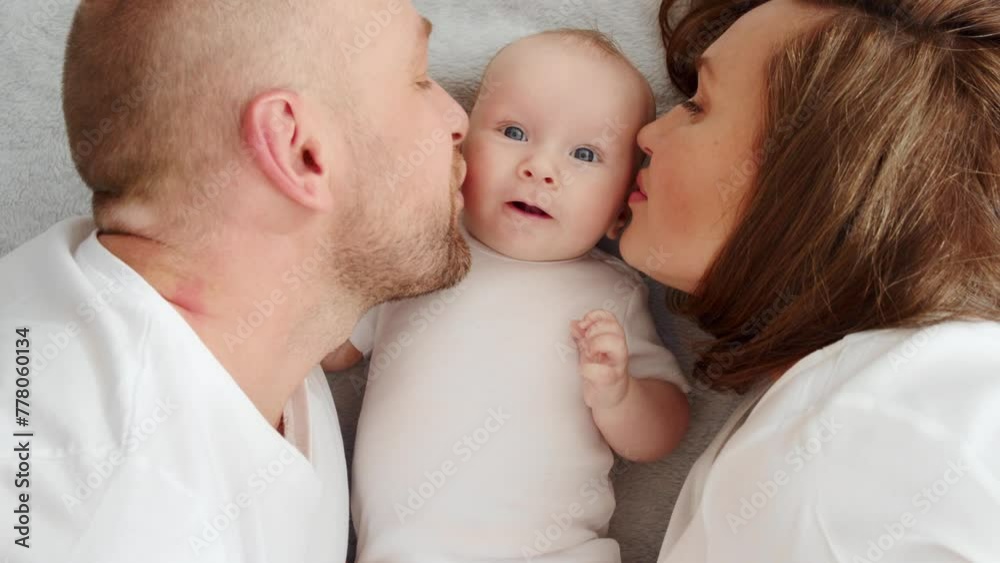 Newborn baby with happy parents, top view. Happy family. Healthy newborn baby in a white t-shirt with mom and dad. Close up Faces of the mother, father and infant baby. Cute Infant boy and parents Newborn baby with happy parents, top view. Happy family. Healthy newborn baby in a white t-shirt with mom and dad. Close up Faces of the mother, father and infant baby. Cute Infant boy and parents