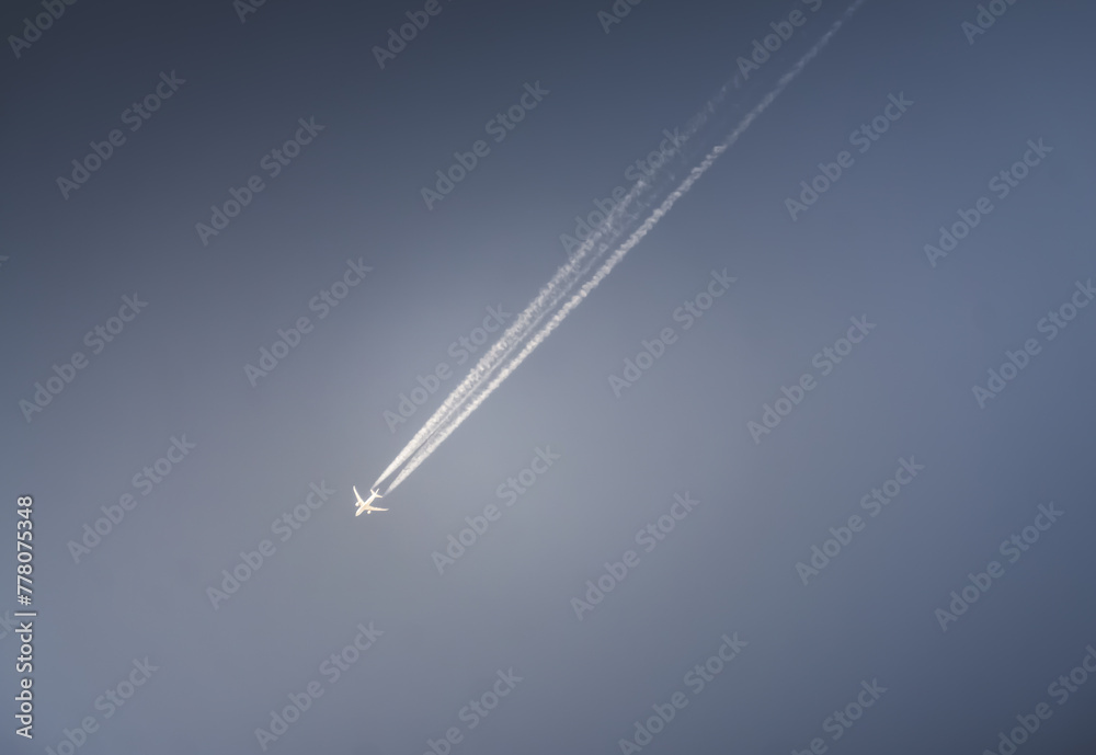 An airplane flies in a blue cloudy sky leaving a contrail, abstraction for background An airplane flies in a blue cloudy sky leaving a contrail, abstraction for background