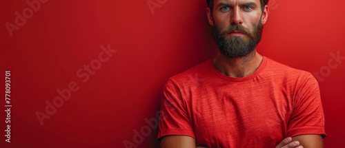 a man with a beard standing in front of a red wall with his hands folded in front of his chest.