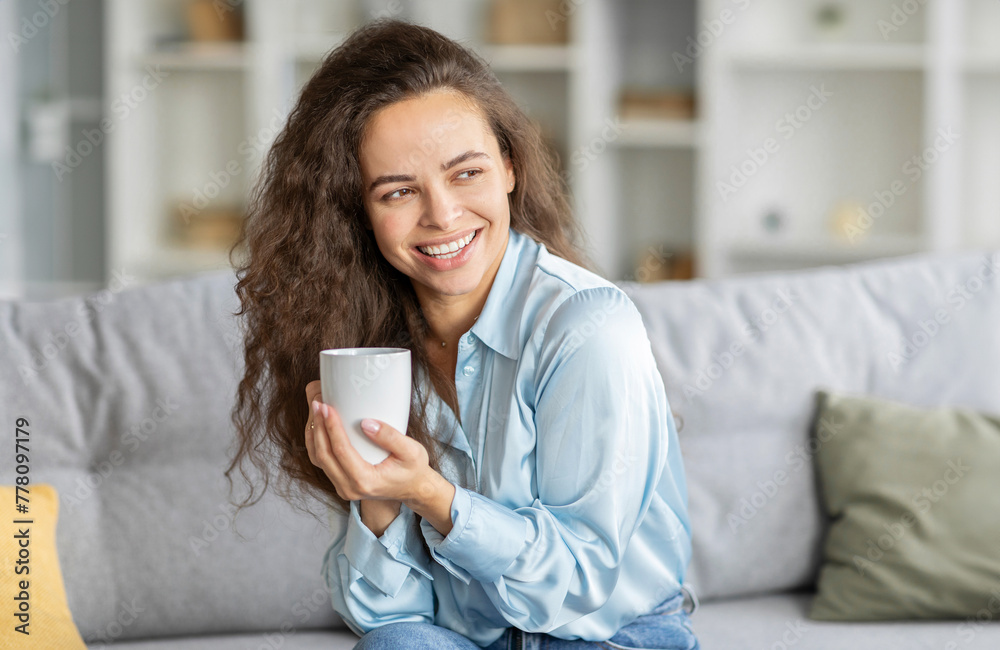 Excited european woman enjoying lazy morning with coffee in living room, lady relaxing on couch with cup of hot drink at home Excited european woman enjoying lazy morning with coffee in living room, lady relaxing on couch with cup of hot drink at home