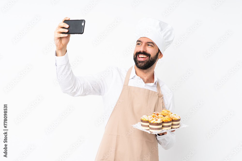 Young man holding muffin cake over isolated white background making a selfie Young man holding muffin cake over isolated white background making a selfie