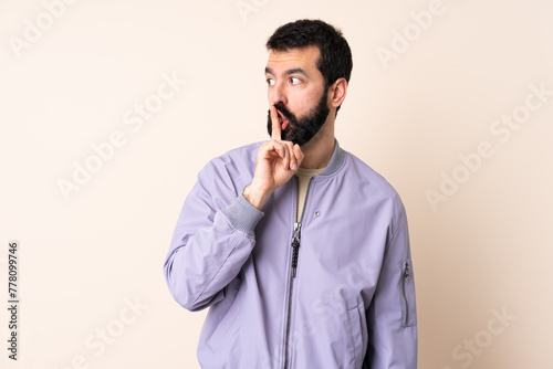 Caucasian man with beard wearing a jacket over isolated background showing a sign of silence gesture putting finger in mouth