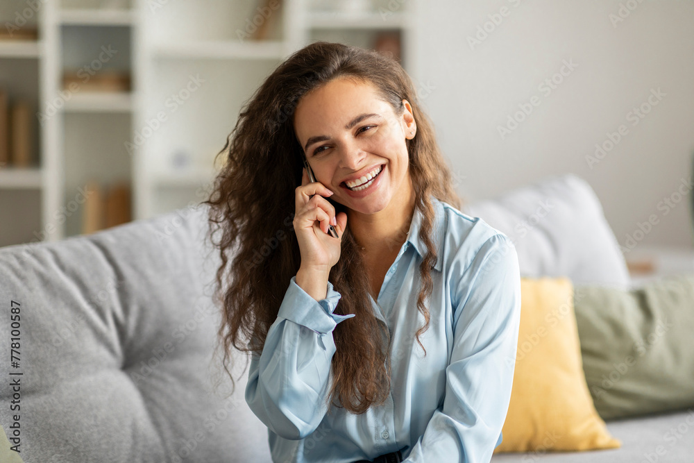 Good talk on mobile. Happy young woman talking on cellphone while sitting on sofa at home and smiling at camera Good talk on mobile. Happy young woman talking on cellphone while sitting on sofa at home and smiling at camera