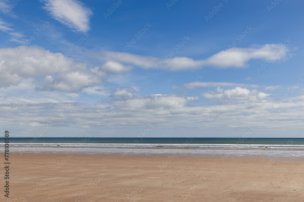This image captures the serene expanse of St Andrews Beach in Scotland, showcasing a wide stretch of golden sand under a vast sky adorned with fluffy clouds