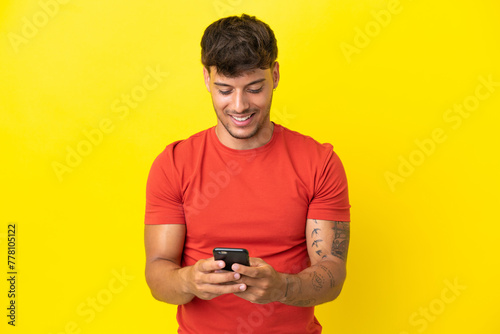 Young caucasian handsome man isolated on yellow background sending a message with the mobile © luismolinero