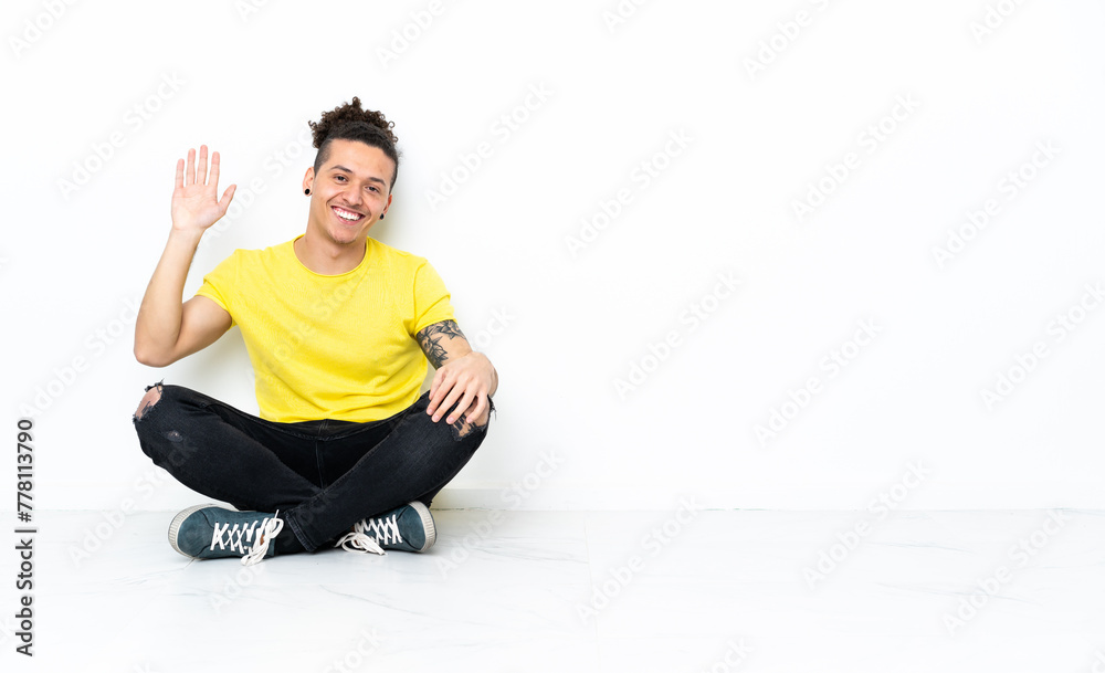 Caucasian man sitting on the floor saluting with hand with happy expression