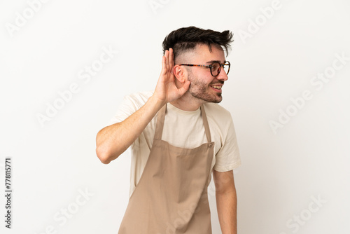 Restaurant waiter caucasian man isolated on white background listening to something by putting hand on the ear © luismolinero