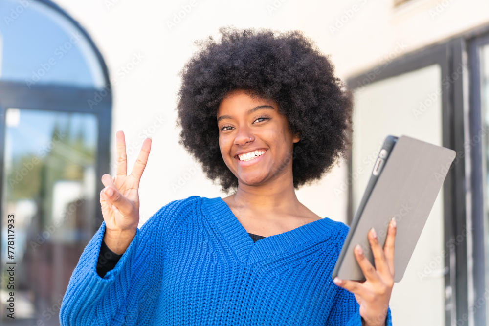 African American girl holding a tablet at outdoors smiling and showing victory sign African American girl holding a tablet at outdoors smiling and showing victory sign