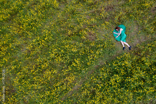 Overhead view of woman laying down on blooming meadow grass field. Spring time outdoor