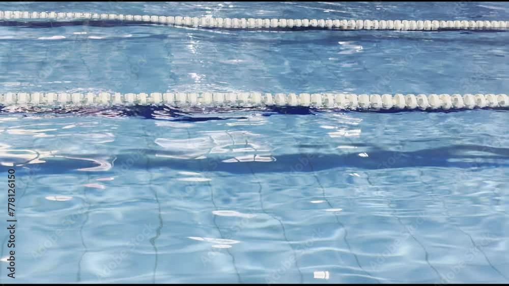 Swimming pool segmented by lane ropes, rippling water reflecting sunlight, embodying themes of sport, fitness, competitive swimming, aquatic exercise and staying active for healthy lifestyle