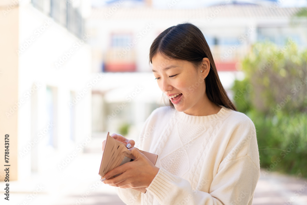 Pretty Chinese woman at outdoors holding a wallet with surprised expression Pretty Chinese woman at outdoors holding a wallet with surprised expression