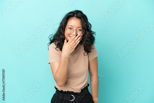 Young asian woman isolated on blue background happy and smiling covering mouth with hand