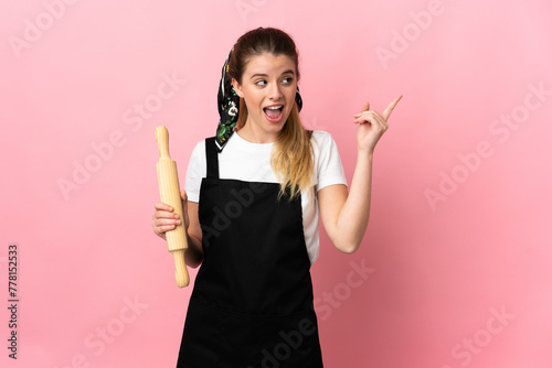 Young blonde woman holding a rolling pin isolated on pink background intending to realizes the solution while lifting a finger up
