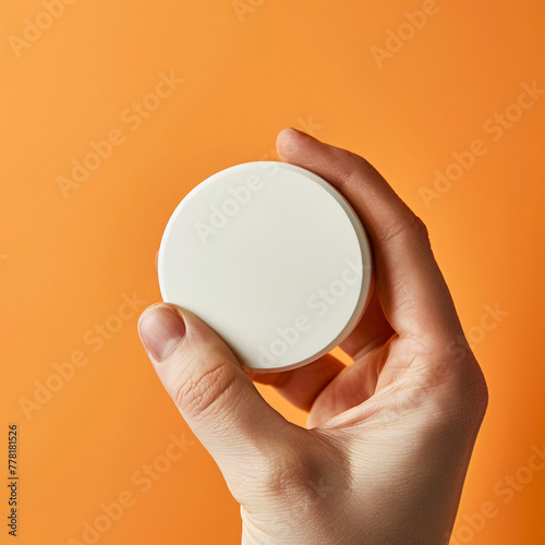 Hand holds a white, round object against an orange background. photo