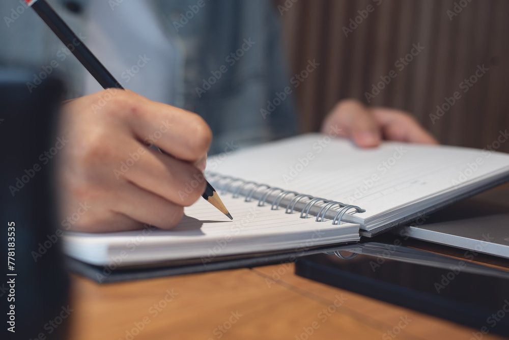 Woman hand writing on notebook and working on laptop computer in office. Student studying online via laptop and noting on notepad, close up. Woman hand writing on notebook and working on laptop computer in office. Student studying online via laptop and noting on notepad, close up.