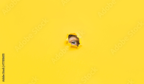 A right eye looking through a hole in a yellow paper. Voyeurism. The man is watching the wife. A curious look. Jealousy, spying on or overhearing the concept. Copy space. photo