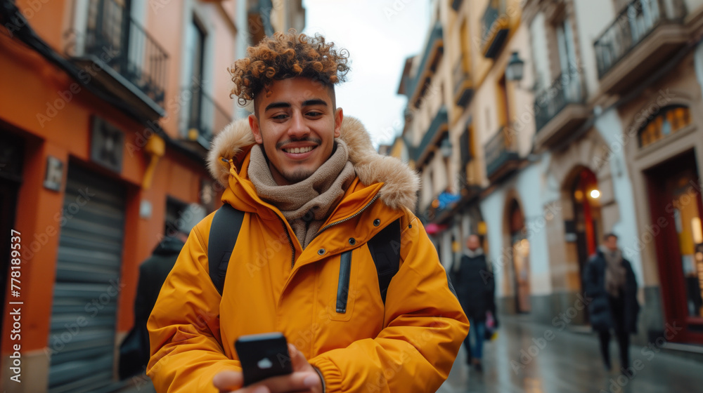 Cheerful young hispanic man smiling while using a smartphone on a bustling city street, clad in a vibrant yellow winter jacket. Cheerful young hispanic man smiling while using a smartphone on a bustling city street, clad in a vibrant yellow winter jacket.