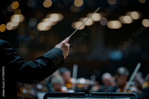 The conductor is leading the orchestra, holding a baton in front, directing the musicians photo