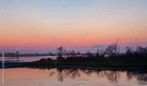 A beautiful sunset over a lake with trees in the background © kmlPhoto