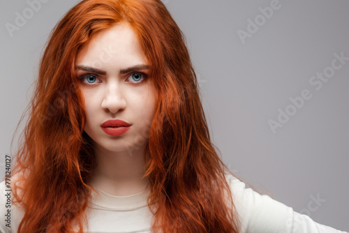 red-haired girl. young beautiful girl model with red long hair and red lush lips stands on a gray background, beauty concept