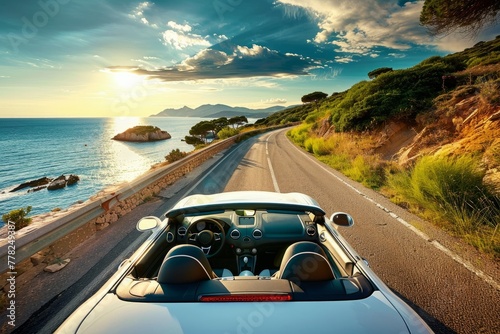 A car is seen driving down a coastal road next to the ocean under a clear sky photo