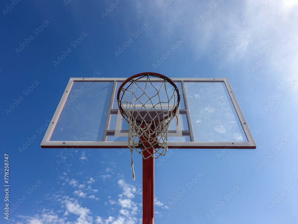 Basketball hoop with net on an outdoor court with sky background from below