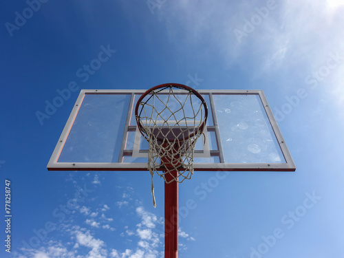 Basketball hoop with net on an outdoor court with sky background from below © snowyns
